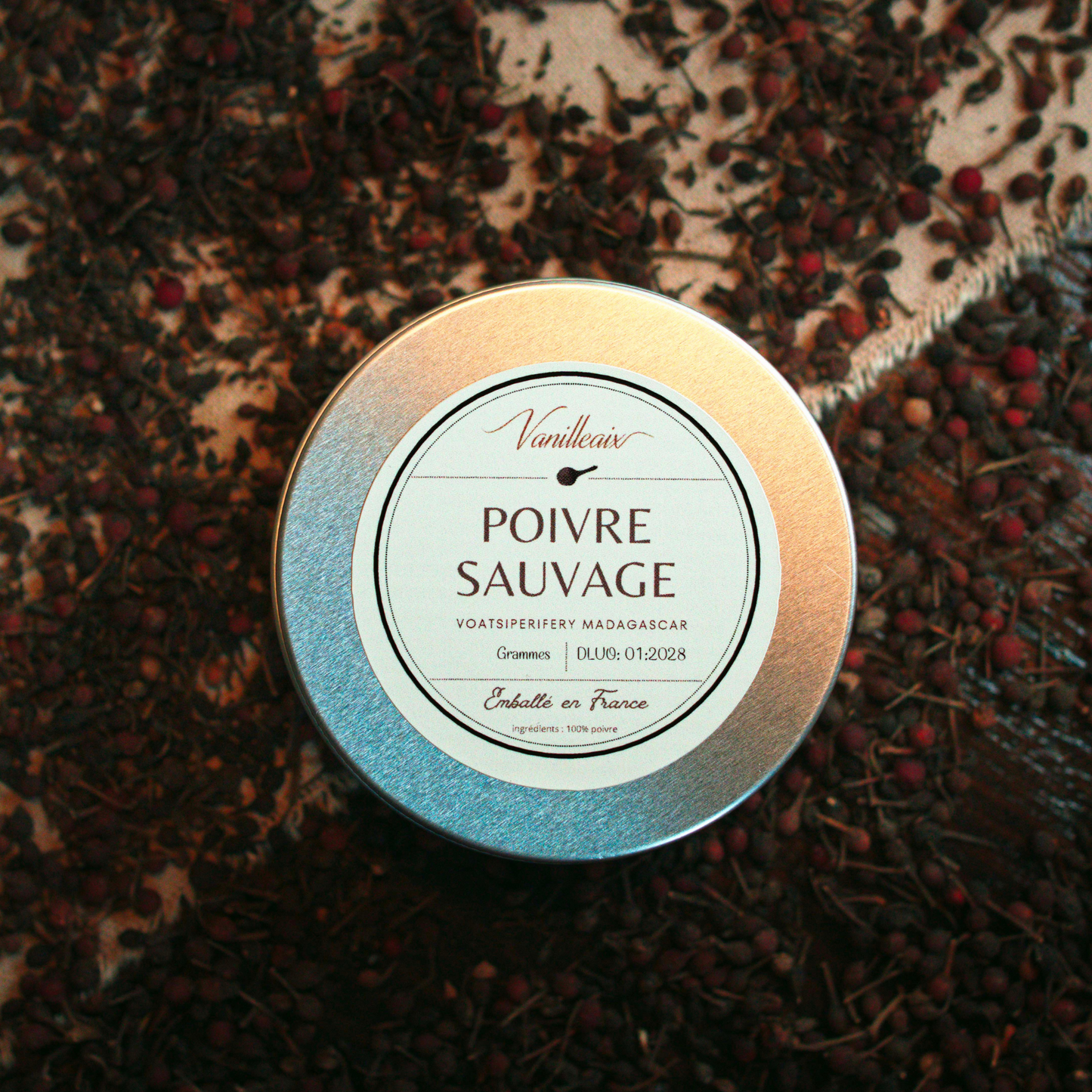 Boîte en aluminium étiquetée « Poivre Sauvage » posée sur un lit de poivre